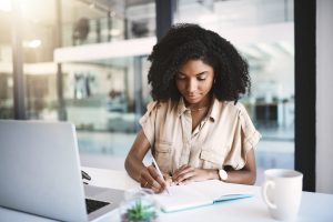 Office, black woman and writer with notebook for writing, notes and information for news article with pen. Workplace, journal and female journalist for planning, reading and research for story.
