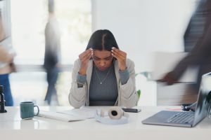 Stress, anxiety and woman at desk in busy office with headache, laptop or deadline crisis. Mental health, business and professional girl with computer, paperwork and burnout chaos at creative startup.